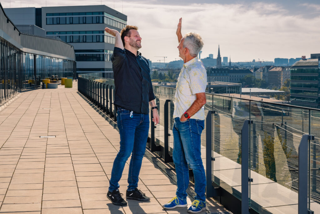 Die zwei Geschäftsführer der JobCloud HR Tech stehen auf einer Terrasse und klatschen gegenseitig in die Hände